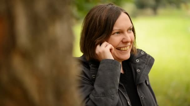 Schöne junge erwachsene Frau, die im Herbstpark mit dem Smartphone spricht — Stockvideo