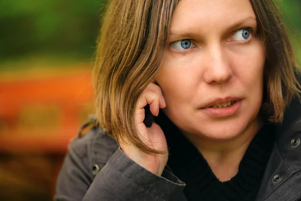 Woman with serious face expression talking on phone in park — Stock Photo, Image