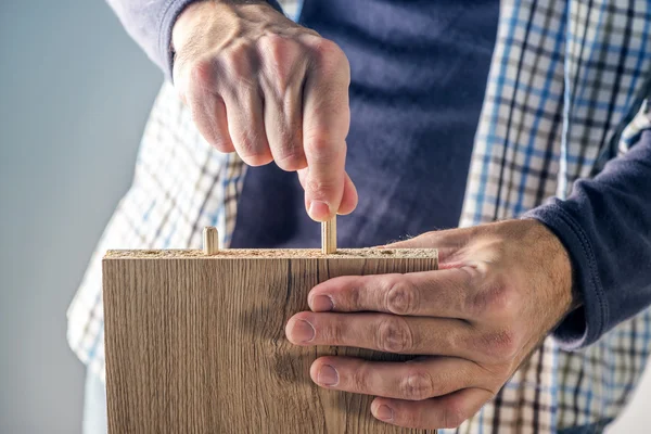 Мужчина собирает мебель дома, рука с деревянными штифтами — стоковое фото