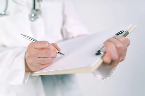 Médica feminina em uniforme branco escrevendo em papel de prancheta — Fotografia de Stock