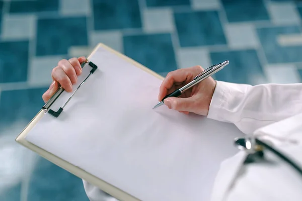 Femme médecin en blanc uniforme écriture sur papier presse-papiers — Photo