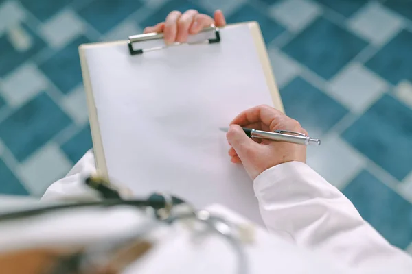 Femme médecin en blanc uniforme écriture sur papier presse-papiers — Photo