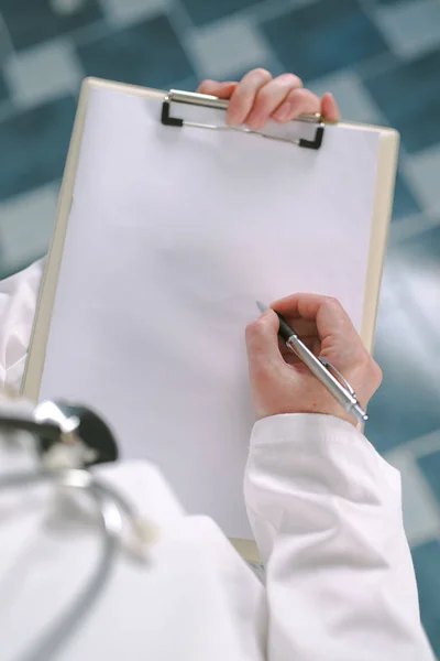 Female doctor in white uniform writing on clipboard paper — Stock Photo, Image