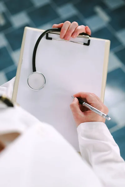 Femme médecin en blanc uniforme écriture sur papier presse-papiers — Photo