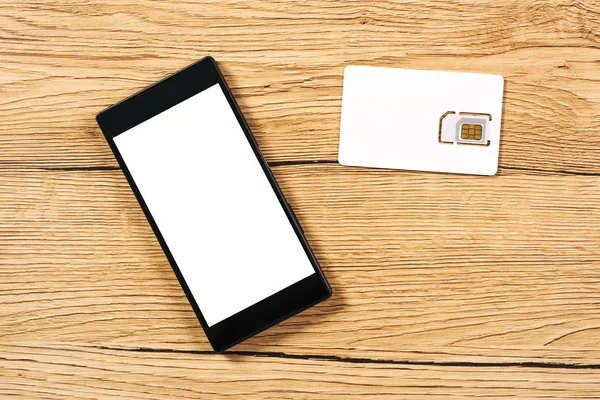 Smartphone und Sim-Karte auf Bürotisch, Draufsicht — Stockfoto