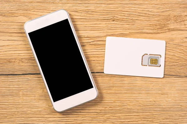 Smartphone and SIM card on office table, top view — Stock Photo, Image