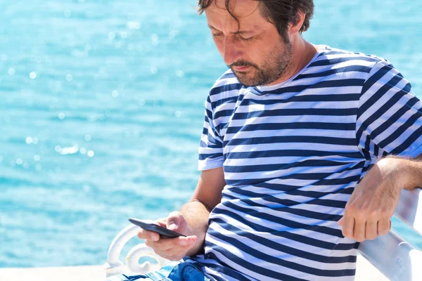 Homem de camisa de marinheiro listrado usando telefone celular no mar — Fotografia de Stock