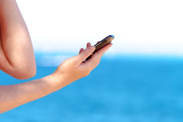 Kaukasiska kvinnliga händer använder mobiltelefon på seaside semester — Stockfoto