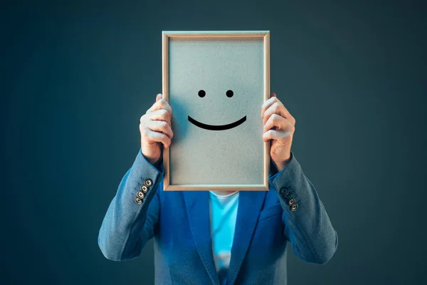 Empresaria es optimista, sosteniendo emoticono sonriente en la cara —  Fotos de Stock