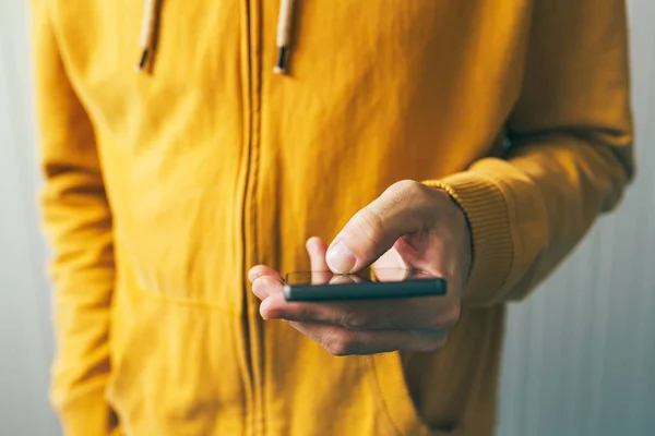 Hombre joven con camisa amarilla usando smartphone — Foto de Stock