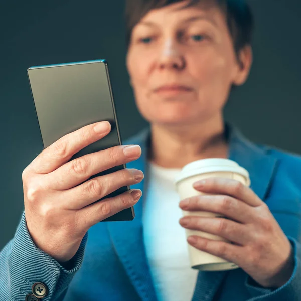 Empresária satisfeita bebendo café para ir e olhando móvel — Fotografia de Stock