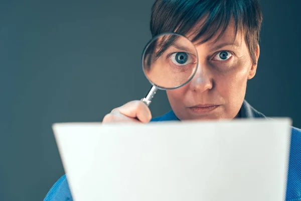 Жіночий податковий інспектор дивиться на документ зі збільшувальним склом — стокове фото