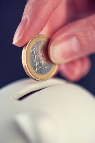 Женщина кладет одну монету евро в копилку — стоковое фото