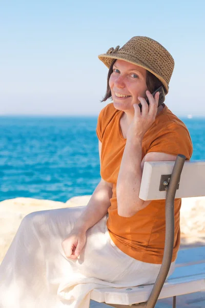 Prachtige volwassen Kaukasische vrouw met behulp van mobiele telefoon op zee va — Stockfoto