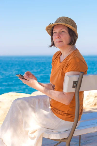 Prachtige volwassen Kaukasische vrouw met behulp van mobiele telefoon op zee va — Stockfoto