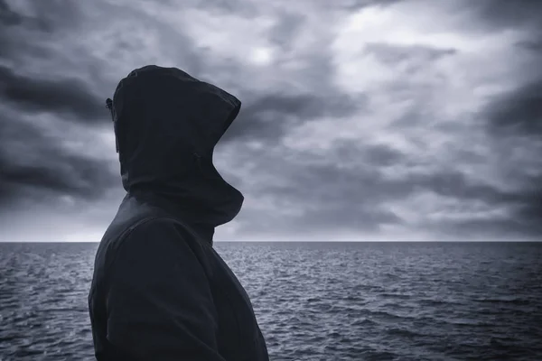 Pessoa encapuzada sem rosto olhando para o horizonte sobre a água do mar — Fotografia de Stock