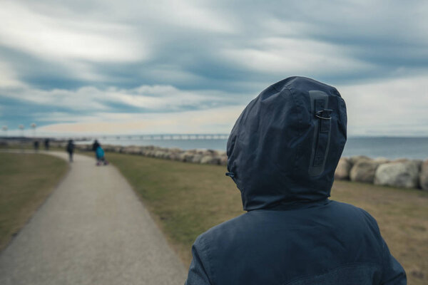 Lonely hooded female person from behind standing at seashore