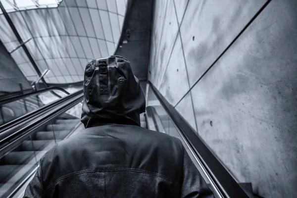 Неузнаваемый человек в капюшоне на движущемся эскалаторе — стоковое фото