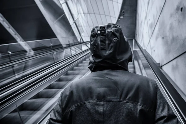 Oigenkännlig hooded person på rörliga rulltrappa — Stockfoto