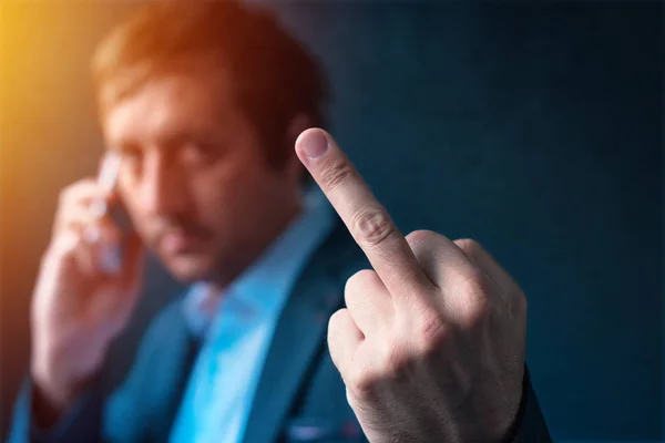 Грубый бизнесмен разговаривает по телефону и показывает средний палец — стоковое фото