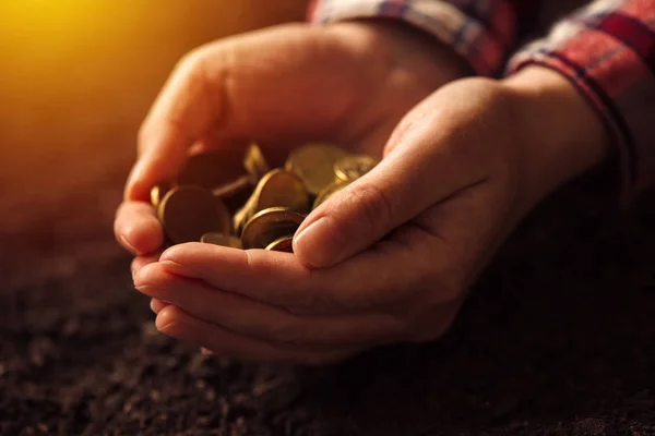 Farmer with handful of coins over soil land — Stock Photo, Image
