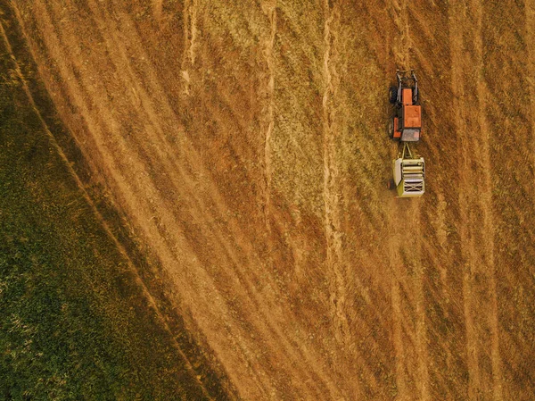 Luftaufnahme eines Traktors, der Heuballen auf einem Feld rollt — Stockfoto