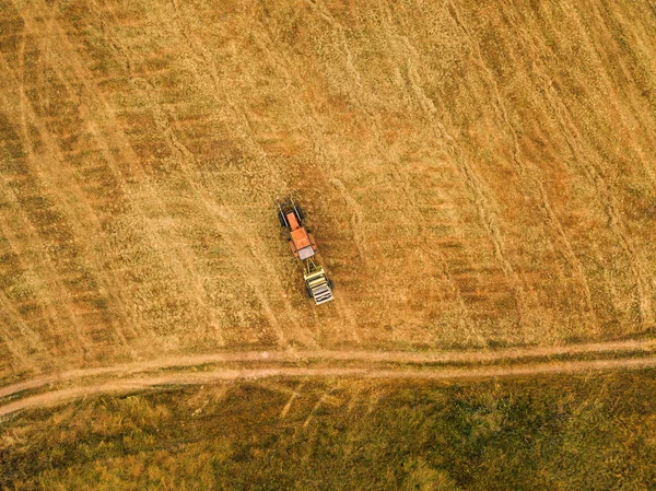 Luftaufnahme eines Traktors, der Heuballen auf einem Feld rollt — Stockfoto