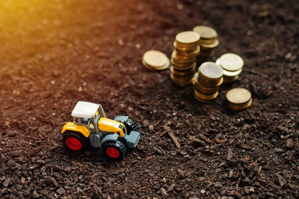 Zabawka ciągnika rolniczego i złote monety na ziemi żyznej gleby — Zdjęcie stockowe