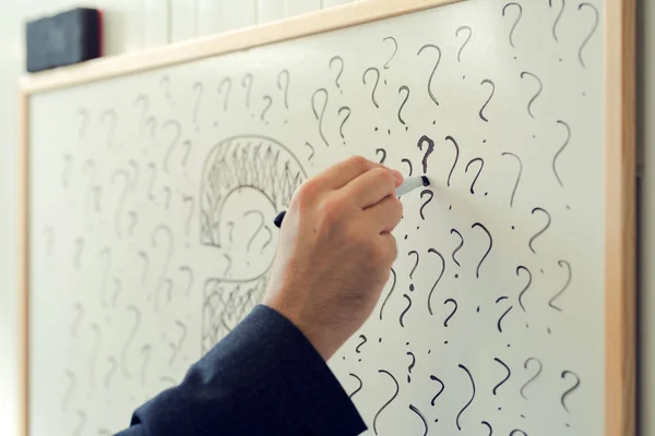Businessman sketching many question marks on office whiteboard — Stock Photo, Image