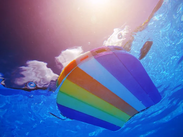 Planche de natation en styromousse à motif arc-en-ciel flottant au bord de la piscine wa — Photo