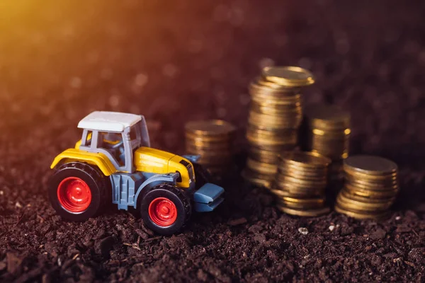 Сельскохозяйственные тракторные игрушки и золотые монеты на плодородной почве — стоковое фото