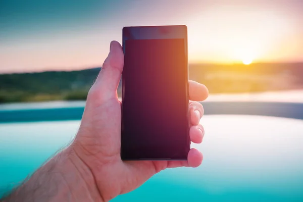 Мужчина держит мобильный телефон у бассейна на закате — стоковое фото