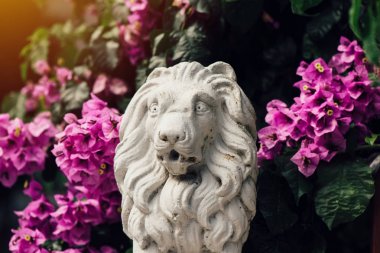 Aslan çiçekler arasında küçük beton heykel