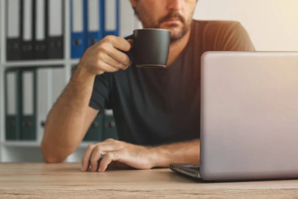 Pití kávy a při pohledu na obrazovku notebooku na volné noze — Stock fotografie
