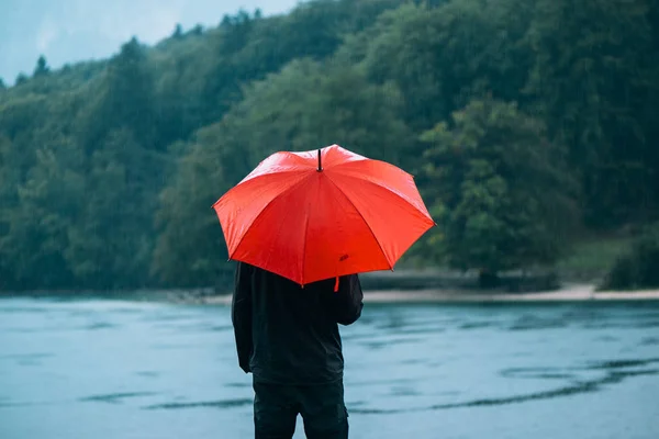 Hombre con paraguas rojo contempla la lluvia —  Fotos de Stock