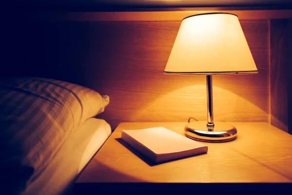 Kniha a lampu na nočním stolku v hotelovém pokoji — Stock fotografie
