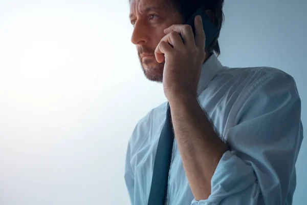 Podnikatel, stojící vedle okna kanceláře a mluví na mobil — Stock fotografie
