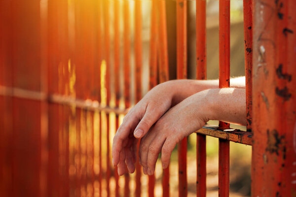 Female hands behind prison yard bars