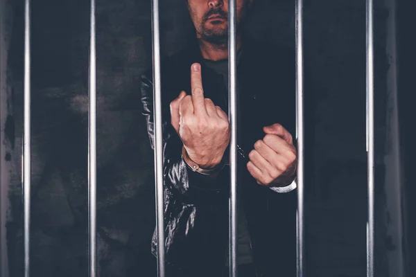 Handcuffed man behind prison bars giving middle finger — Stock Photo, Image