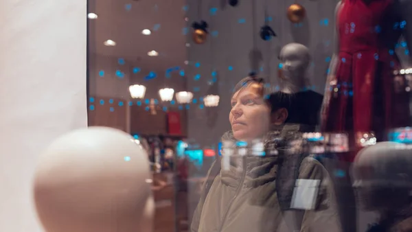 Doordachte vrouw kijkt nacht door etalage — Stockfoto