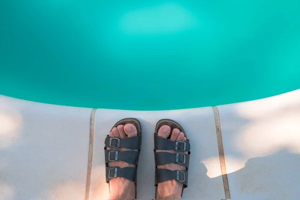 Bare male feet in slippers by the poolside — Stock Photo, Image