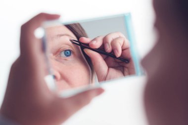 Pencereden kaş yolan bir kadın.