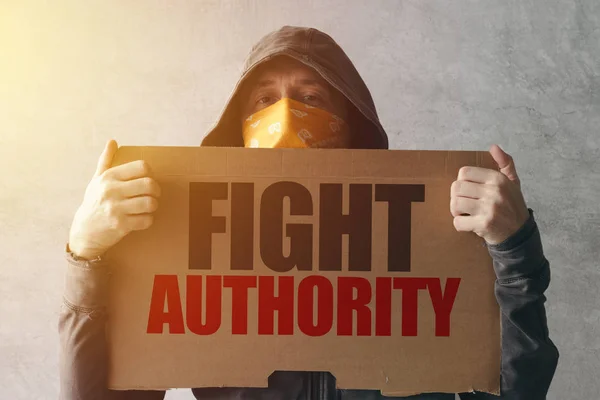 Hooded activist protestor holding Fight authority protest sign