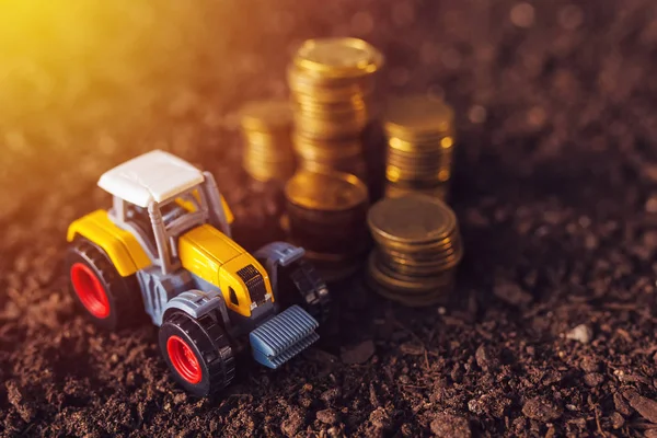 Agricultural tractor toy and golden coins on fertile soil land — Stock Photo, Image