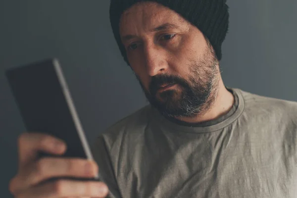 Casual volwassen mannetje met dop kijken naar mobiele telefoon — Stockfoto