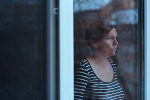 Mujer deprimida de pie junto a la ventana y mirando al exterior —  Fotos de Stock