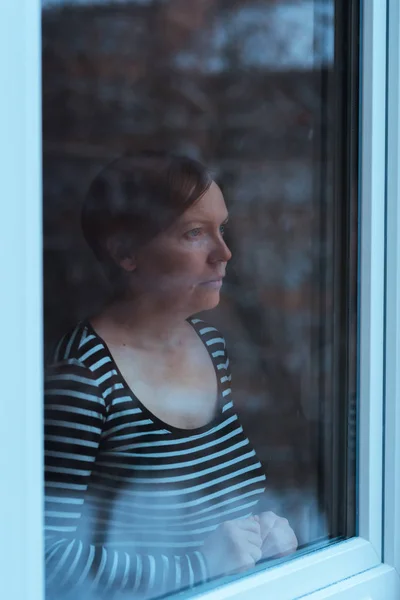 Mujer deprimida de pie junto a la ventana y mirando al exterior —  Fotos de Stock