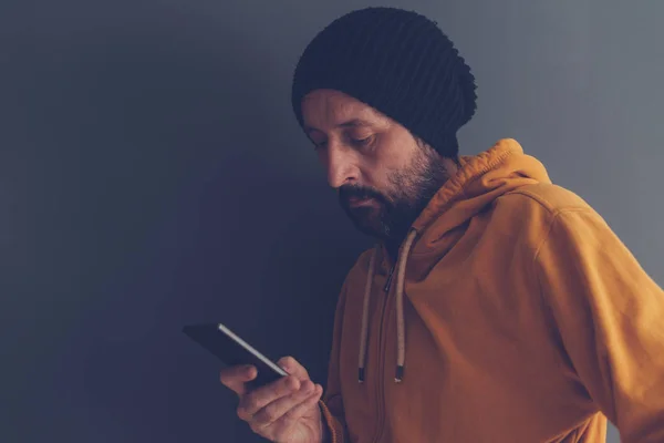 Casual volwassen mannetje met dop kijken naar mobiele telefoon — Stockfoto