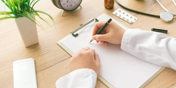 Médica feminina escrevendo notas sobre papel de prancheta durante ex médica — Fotografia de Stock