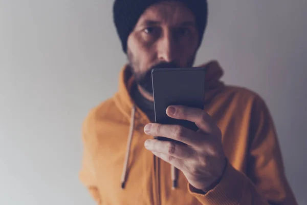 Casual volwassen mannetje met dop kijken naar mobiele telefoon — Stockfoto